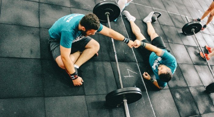 Two friends training together in a gym with a barbell