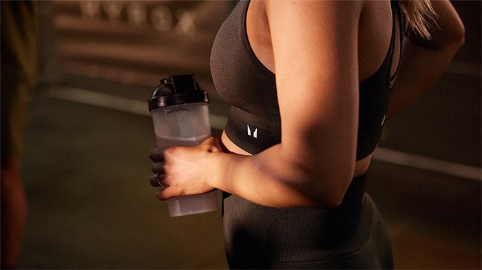 A close up of a young woman mid-exercise holding a Myprotein shaker.