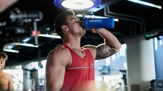 man in gym ctank top drinking fro a protein shaker bottle at the gym